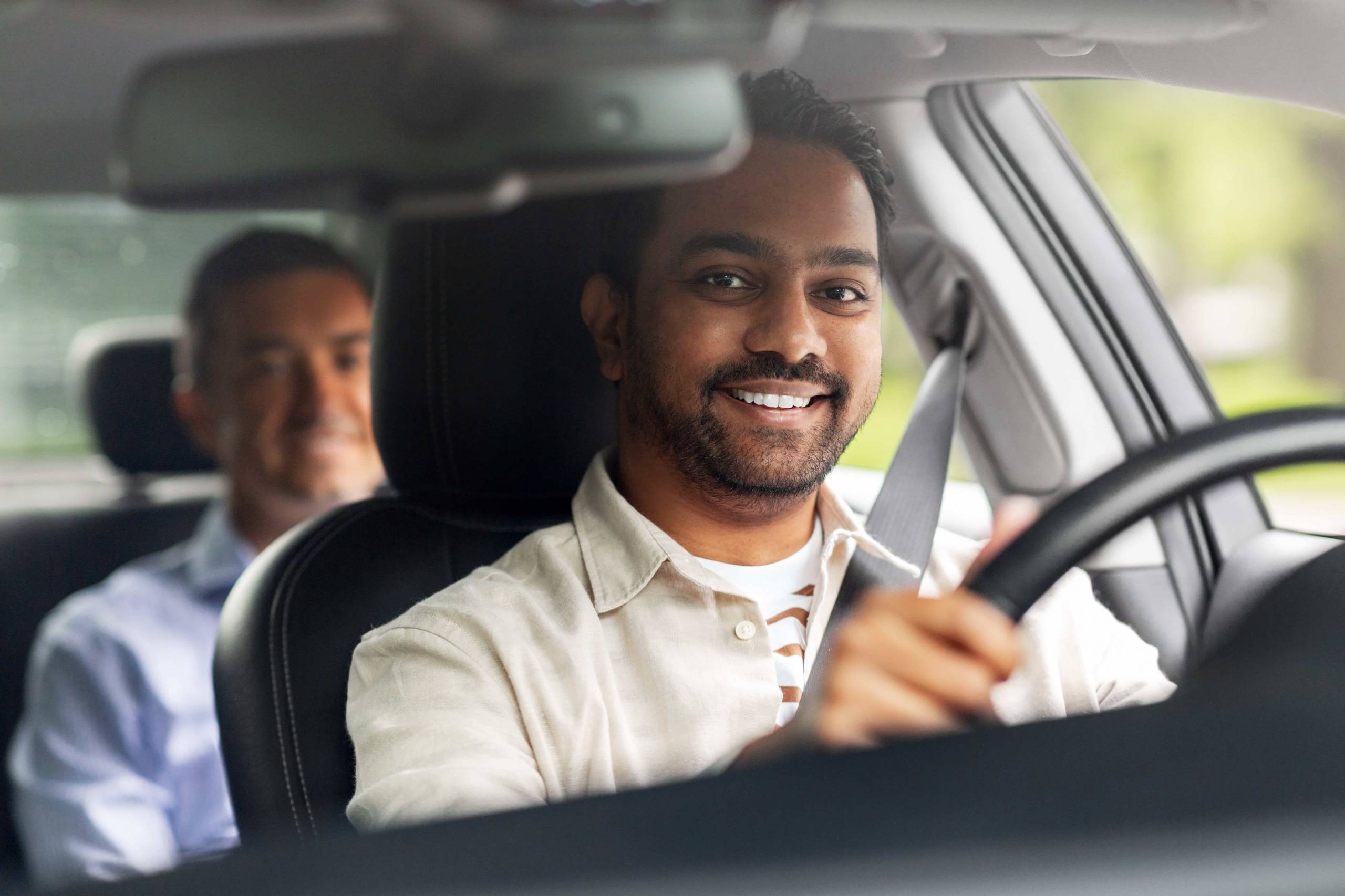 A smiling man driving a car, representing the professionalism of Topcarsminicab Taxi to Heathrow Airport Terminal 3.