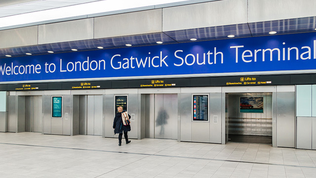 A woman poses by a sign that says Welcome to London Gatwick South Terminal, ready to take a taxi to the North Terminal.