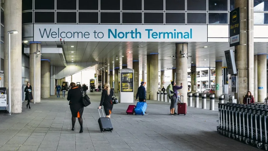 A woman poses by a sign that says Welcome to London Gatwick South Terminal, ready to take a taxi to the North Terminal.